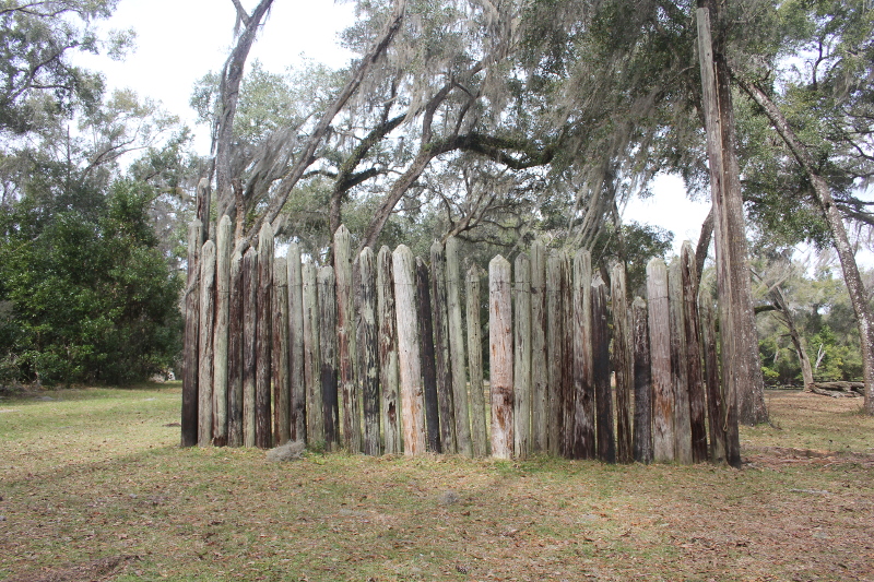 a small picket fence stands on a small hill in front of trees draped with spanish moss