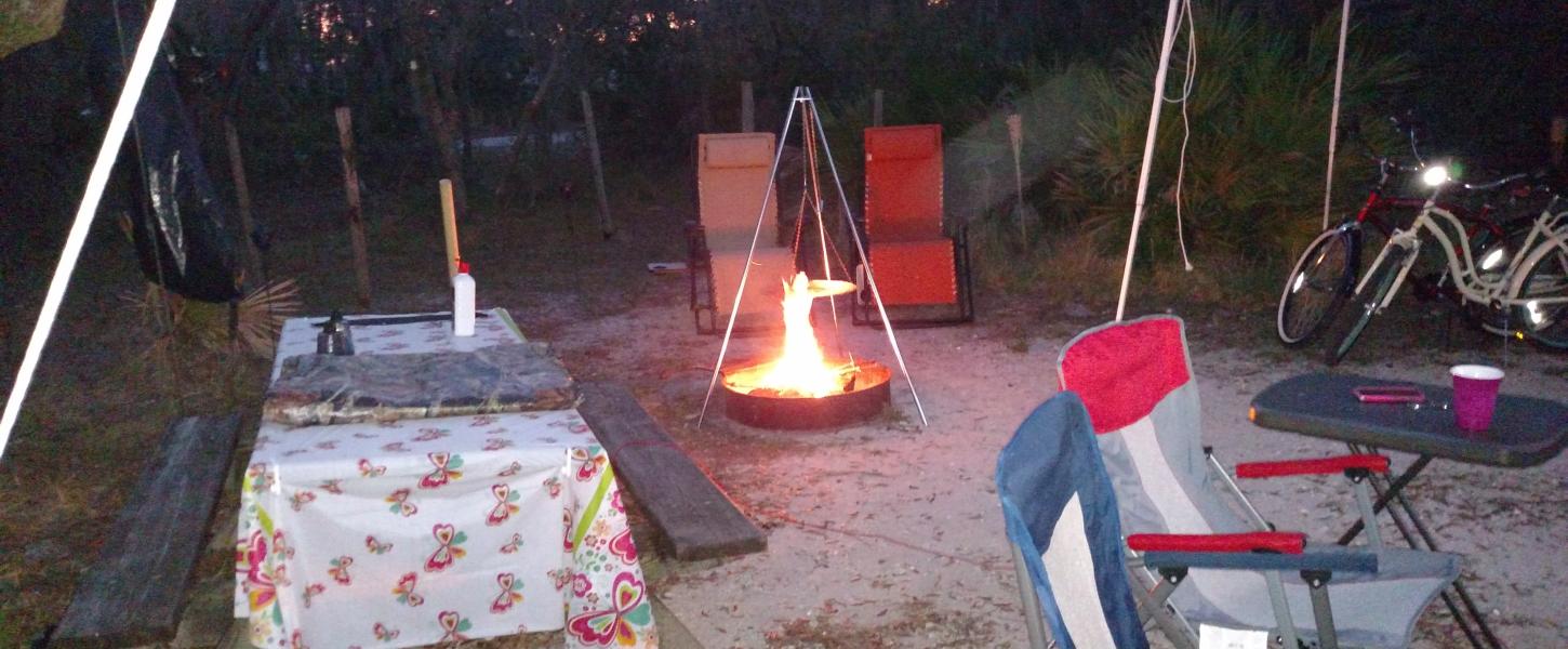 A view of a campsite with table, chairs and camp fire.