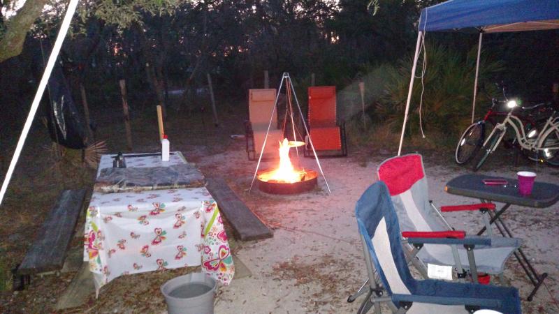 A view of a campsite with table, chairs and camp fire.