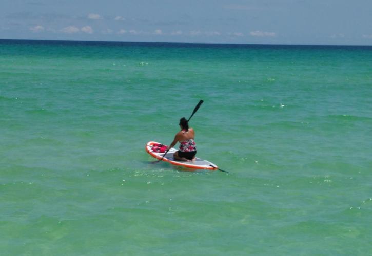 Paddle boarder glides through emerald green waters meeting clear blue skies. 