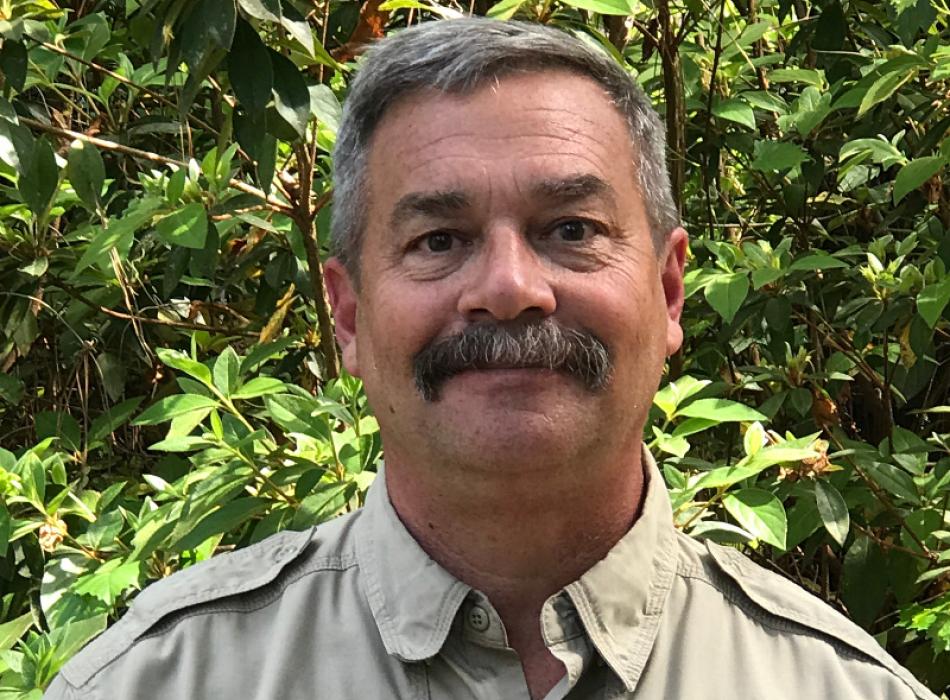a man in park service uniform with a mustache in front of greenery
