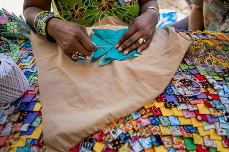 a woman' hands sew a piece of bright blue cloth on a table