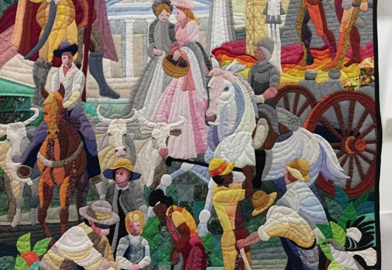 an intricate quilt shows many people and horses from the 1800s in bright colors