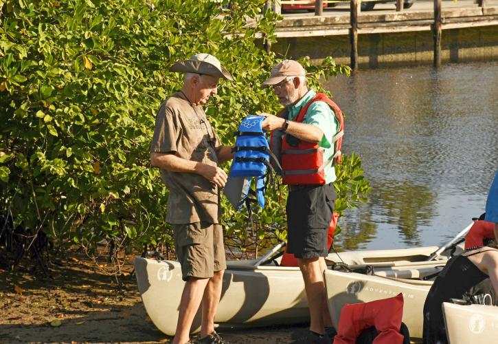 Two men preparing to canoe hold a life vest.