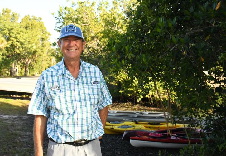 Man wearing blue and white shirt hat standing near canoes.
