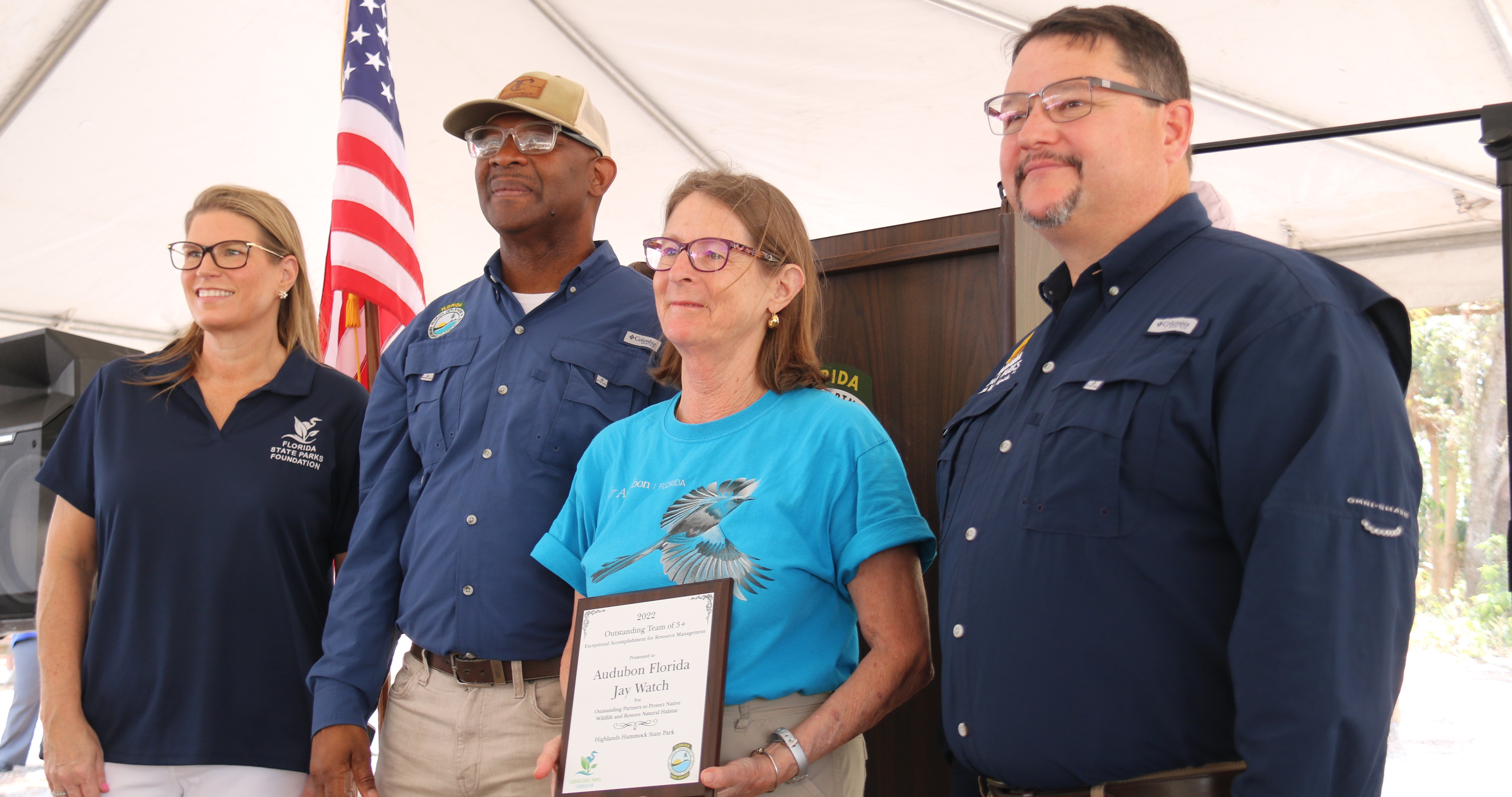 A representative receives the award from Emily Lewis, BJ Givens and Brian Fugate