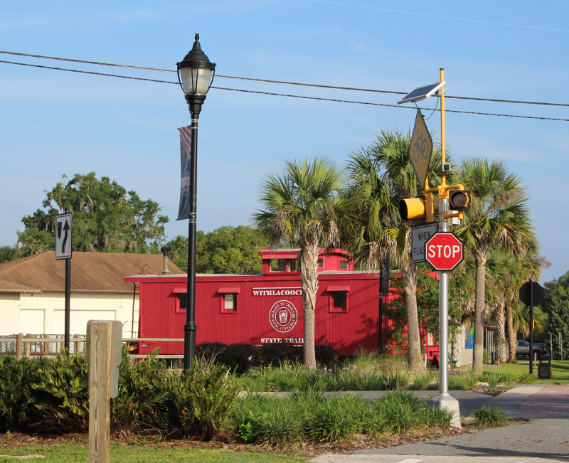 a red caboose sits next to a paved trail in a downtown section of the city of Inverness.