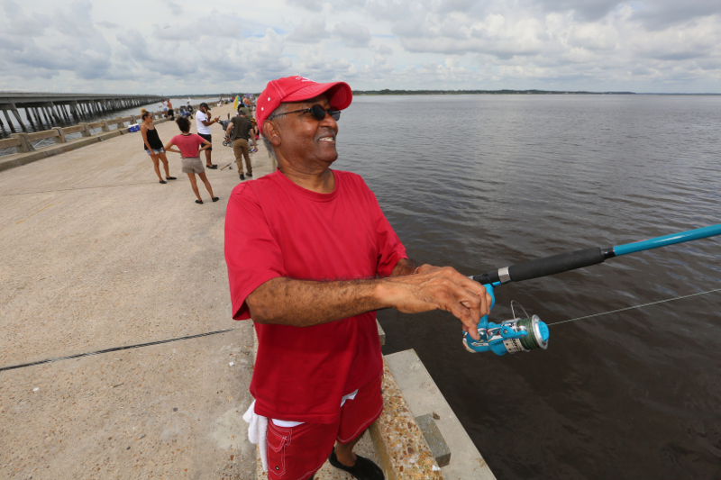 a man dressed in red casts a line off of a concrete bridge over water