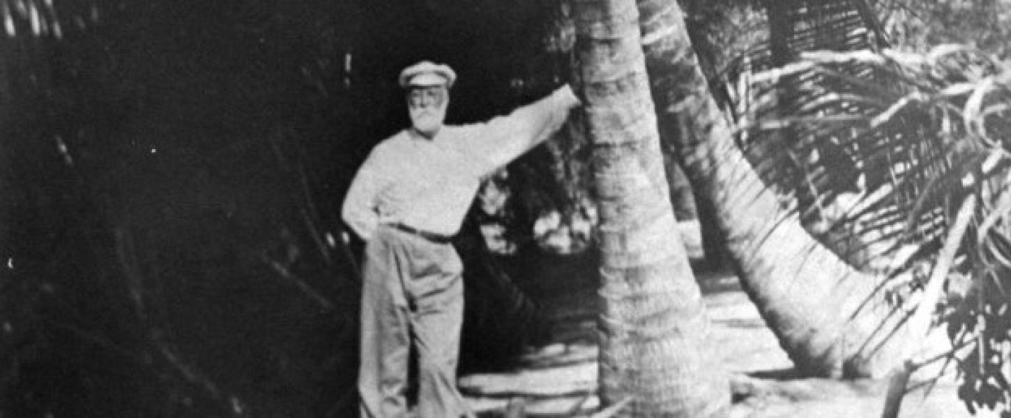 A black and white photo of a man standing next to a large tree.