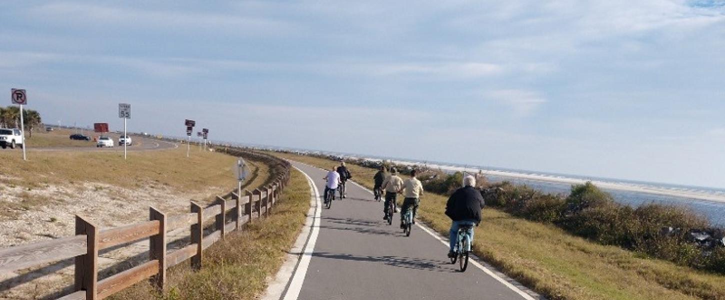 a group of bike riders pedal down a paved trail next to the coastline