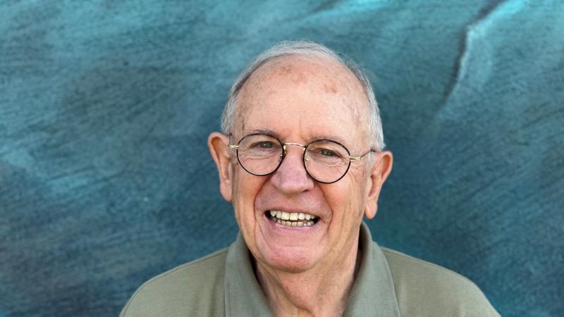 A smiling man wearing glasses, standing in front of a mural.