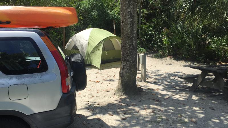 A tent is pitched behind a vehicle with an orange kayak on top.