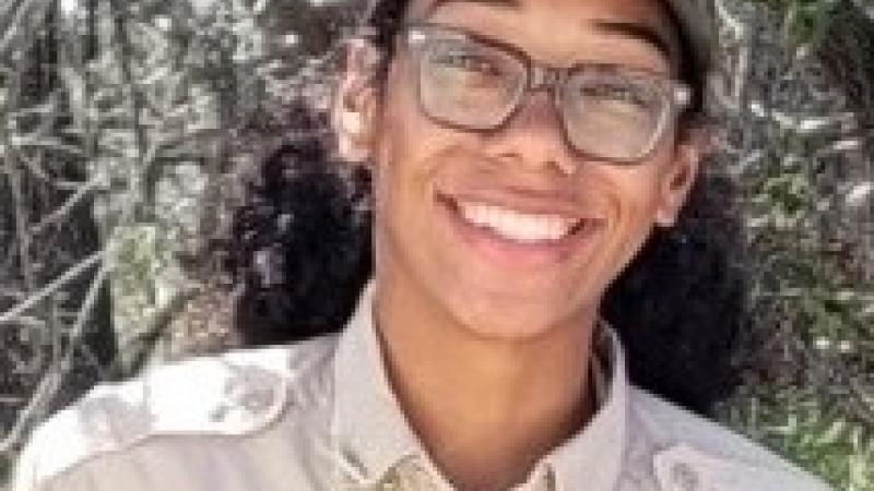 Bryn, smiling in front of wooded area