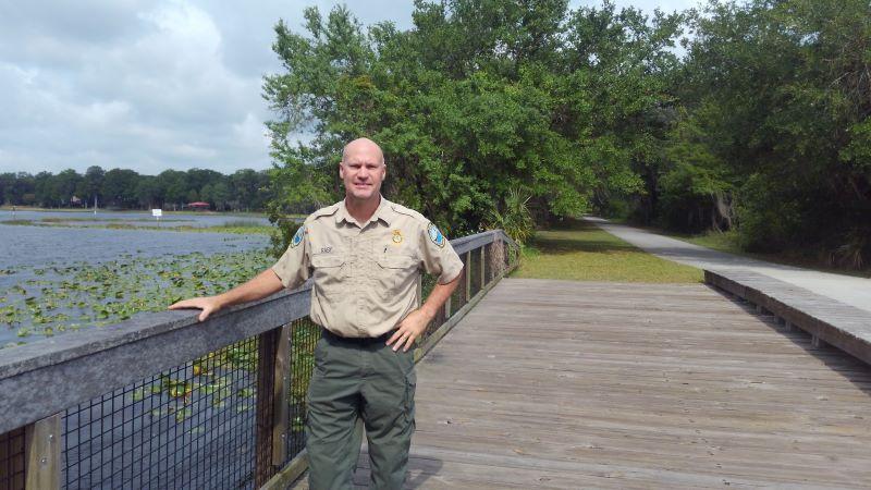 A man in uniform stands on a bridge trail by water