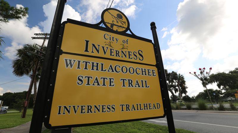 A large yellow and black sign that reads "withlacoochee state trail inverness trailhead"
