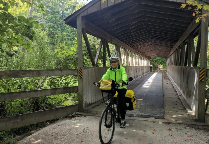 A woman on a bicycle rides under a covered bridge. 