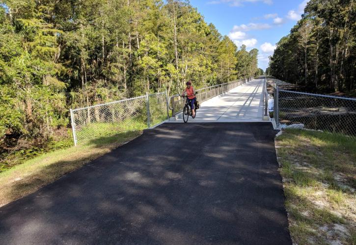 A person on a bicycle rides along a paved trail over a bridge. 