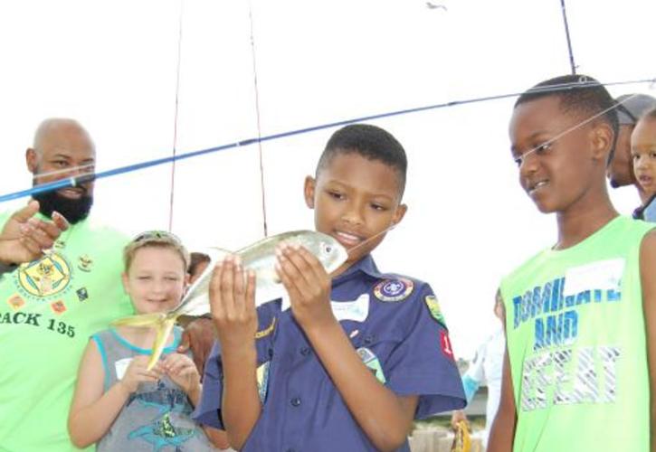 several kids and adult stand around a boy holding a fish