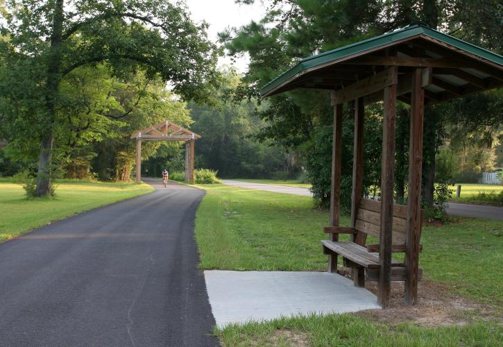 Paved path with bench under covered pavilion. 