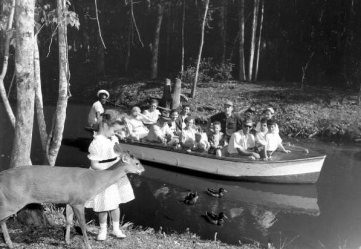 Young girl with a deer near a waterway that has a boat with children