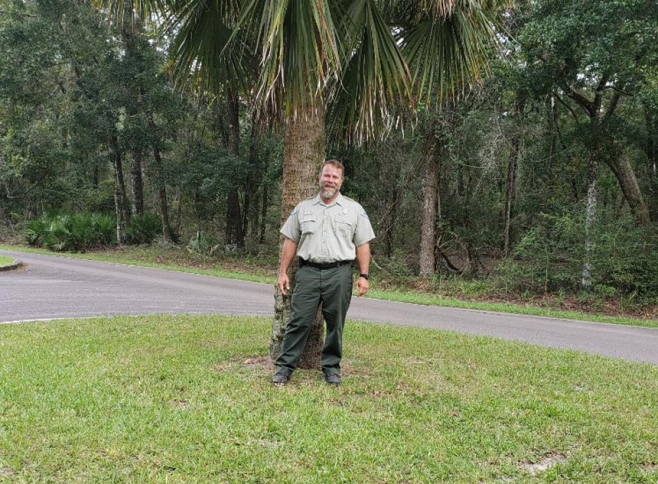 image of bryan summerlin, park ranger at manatee springs state park, standing outside in front of a palm tree.