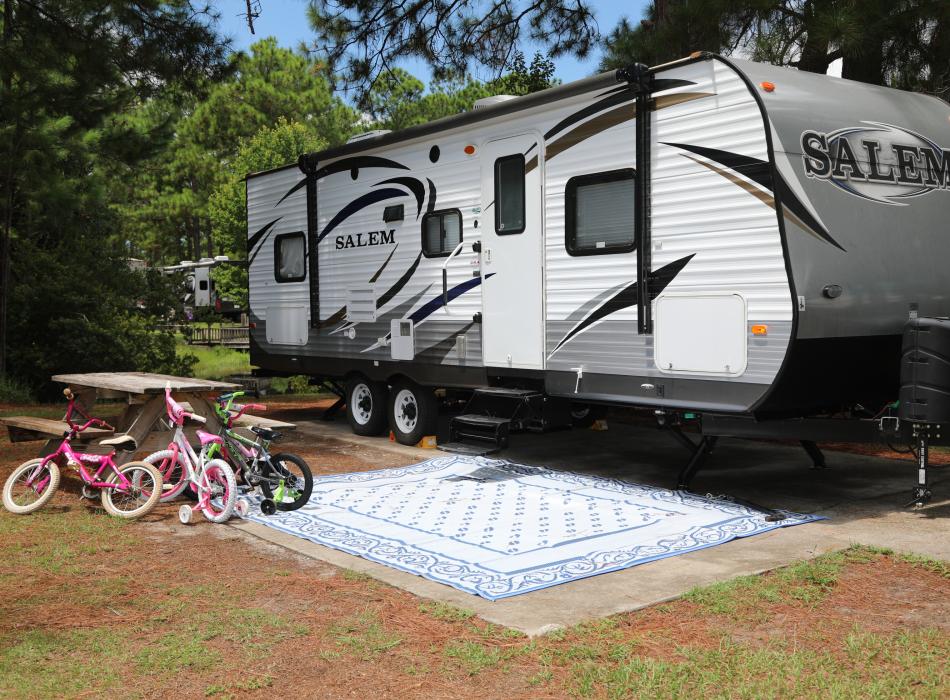 A camper is positioned in the campsite with bicycles propped against at picnic table.
