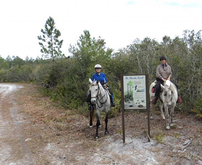 Two riders on horseback next to interpretive sign