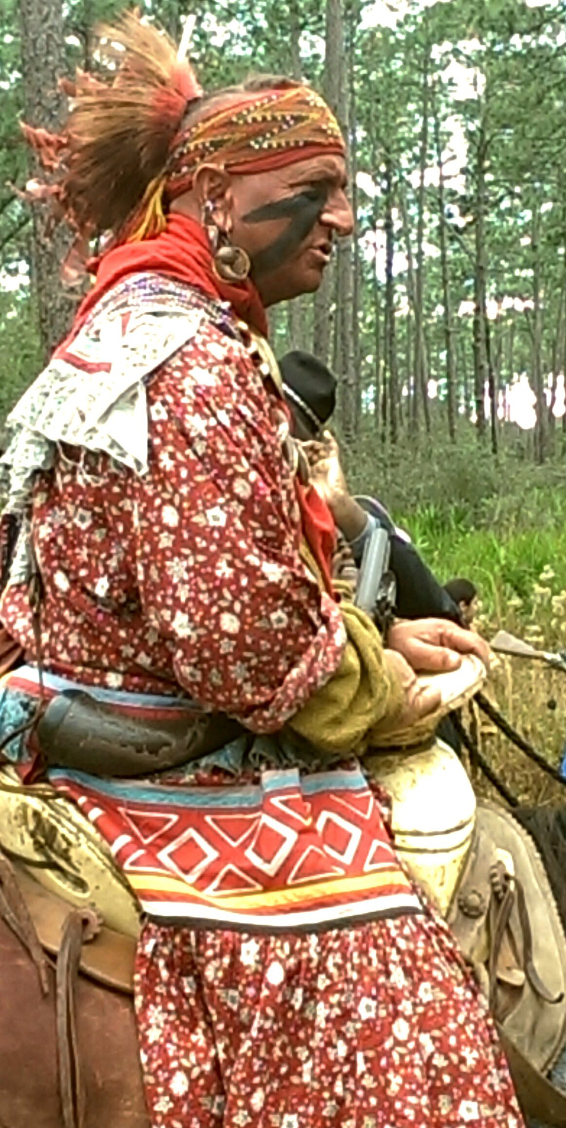 a seminole warrior reenactor in a colorful outfit rides a horse.