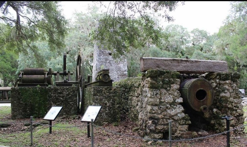 a path winds past a stone structure with iron boilers and interpretive signs