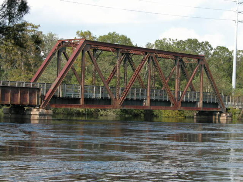 a reddish brown steel span bridge crosses a river