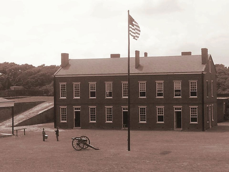 historic image of fort clinch depicting the main building with flagpole, cannon, and two soldiers.
