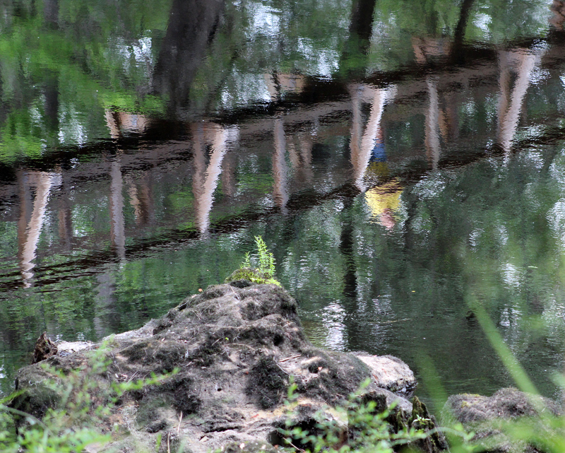 a piece of limestone rock next to water reflecting a bridge