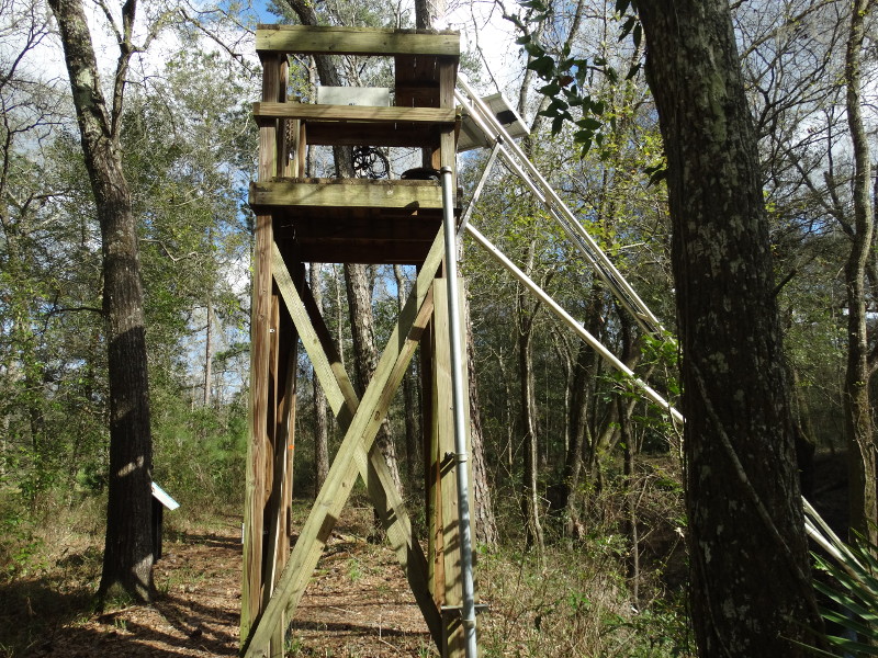 a wooden tower with measuring equipment and pipes stretching into the water.