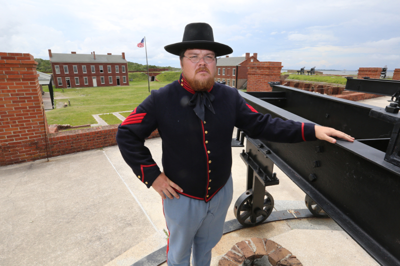 a man in union uniform stands atop the fort walls next to a cannon.
