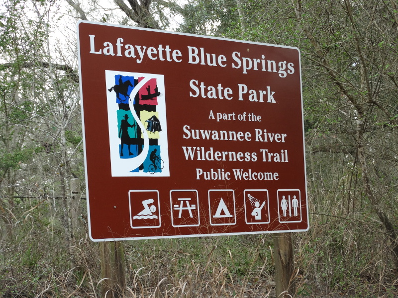 a brown sign reads "lafayette blue springs state park, a part of the suwannee river wilderness trail, public welcome"
