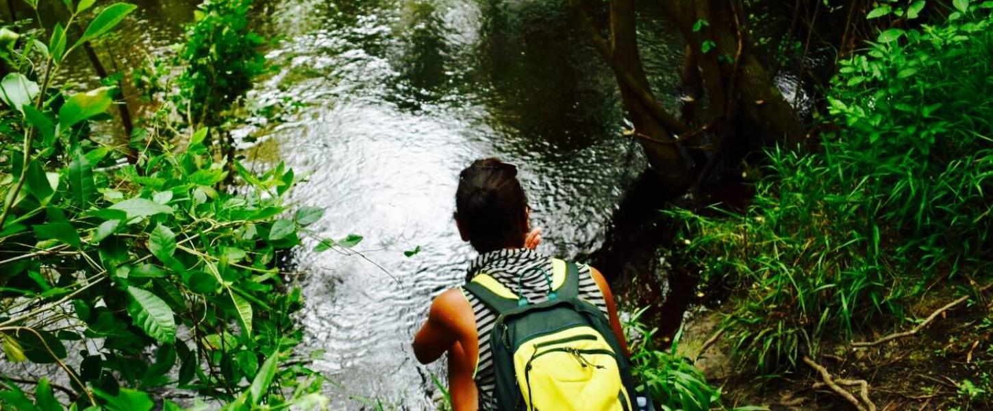 A view of a man sitting by a the river with a yellow backpack.