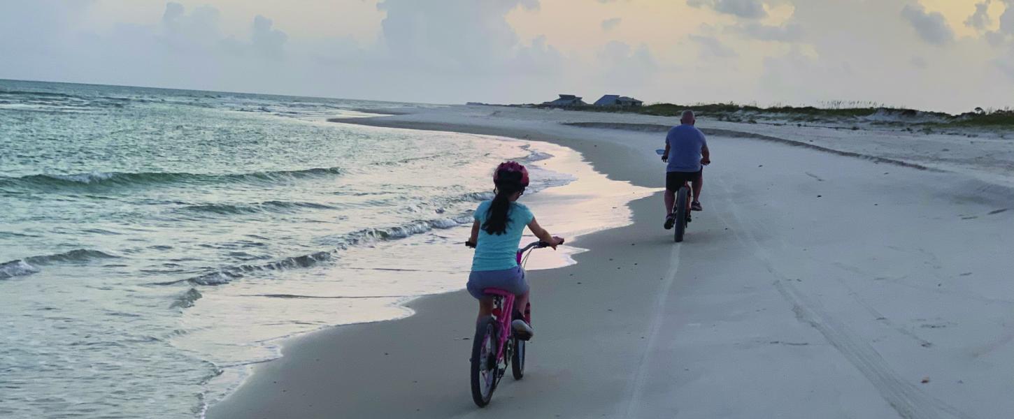 Two people ride bicycles on the beach.