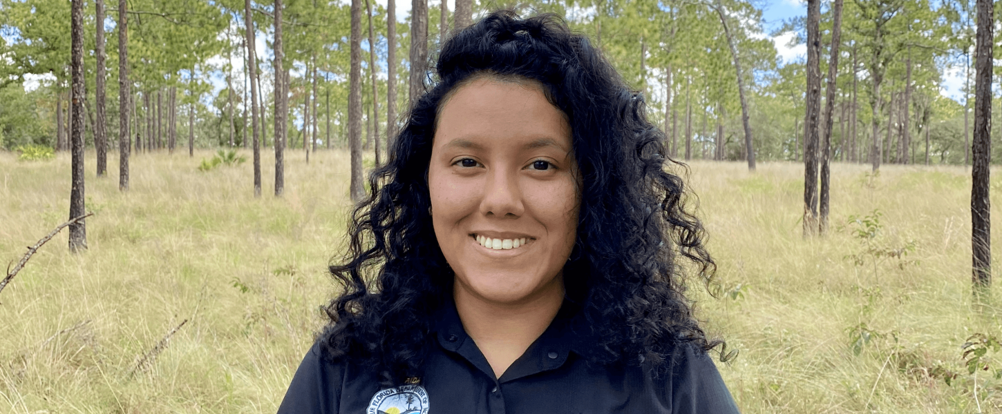 M Gonzalez stands in pine forest.