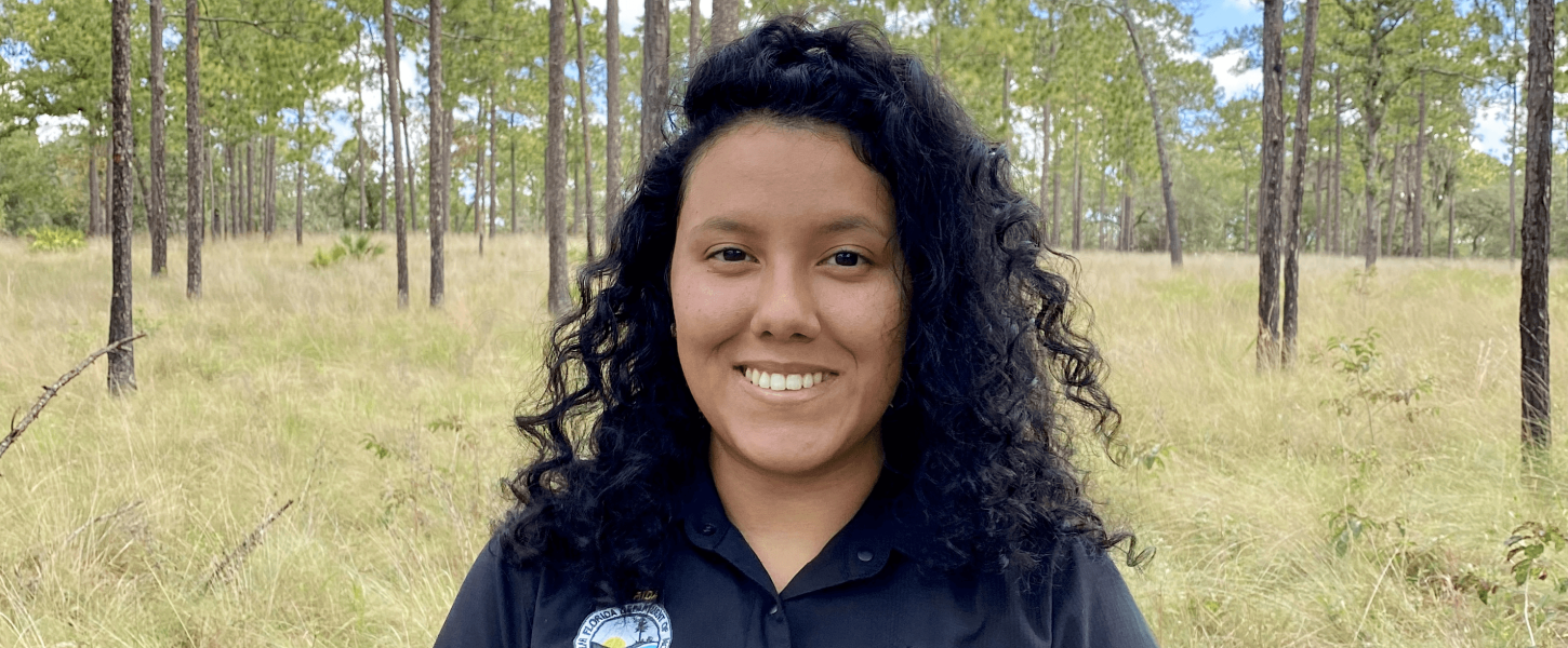 M Gonzalez stands in pine forest. 