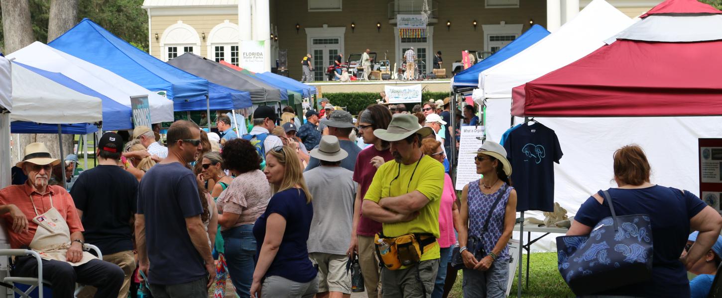 A large crowd between booths at Florida Springsfest 2019 with music stage in background. 