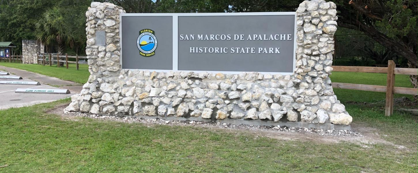 Stone and wood park sign outside San Marcos de Apalche Historic State Park. 