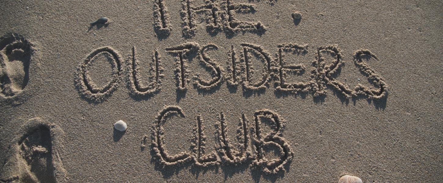 The words "The Outsiders Club" written in sand on the beach. 