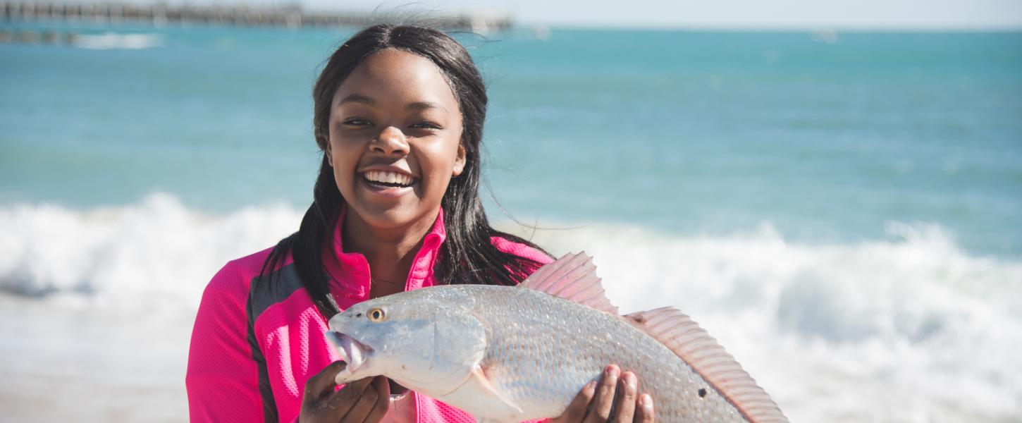 A young woman holds a red drum fish on the beach. 