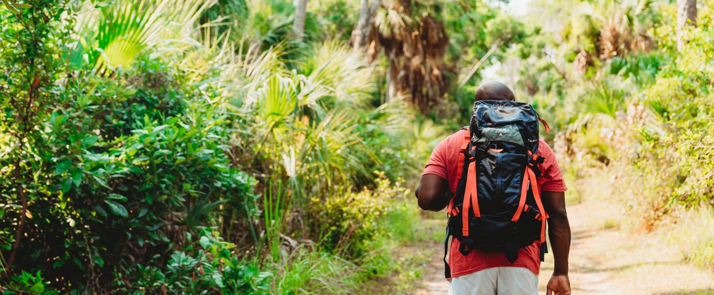 a man has his back turmed, walking on a trail with a backpack.