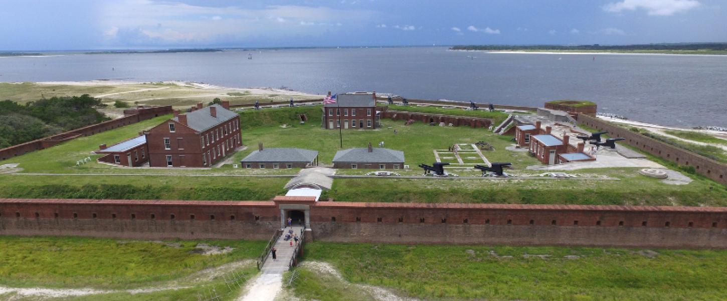 a fort with pentagonal brick walls and numerous building and guns against the backdrop of the ocean.