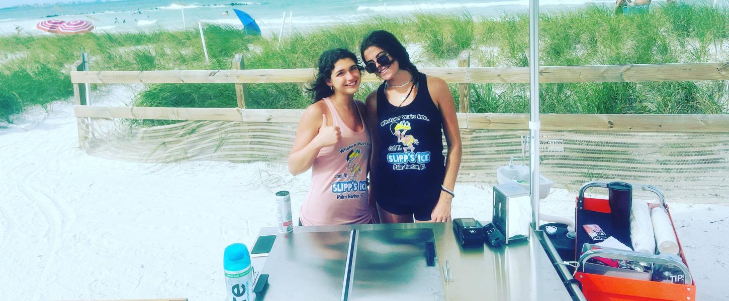 Two women pose with the ice cart at the beach.