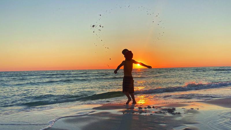 A boy plays by the shoreline at sunset.