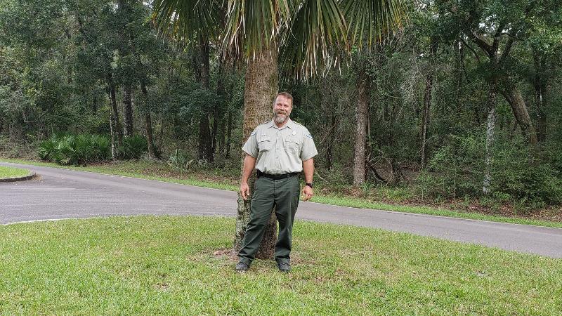 image of bryan summerlin, park ranger at manatee springs state park, standing outside in front of a palm tree.