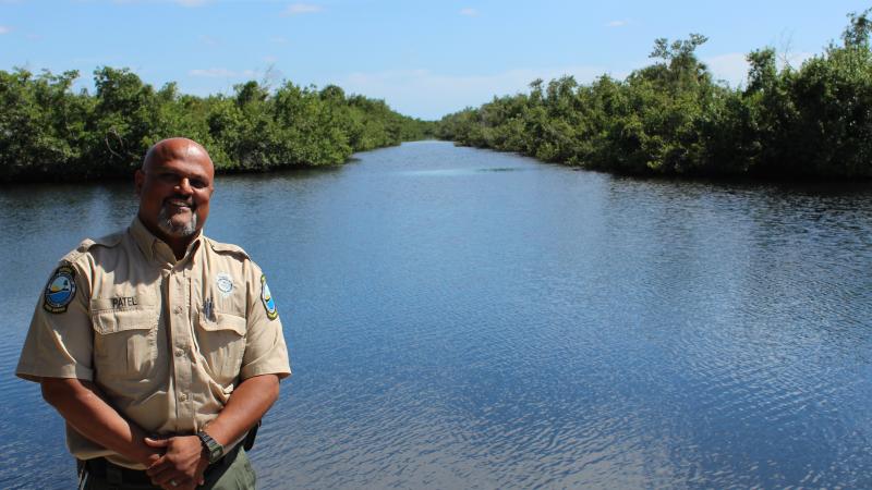 A male biologist in a Florida Park Service uniform stands proudly by a body of water. 