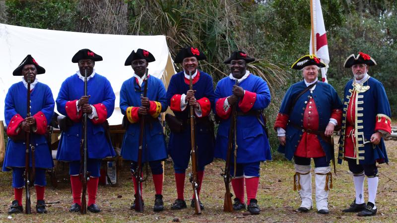 A group of men standing shoulder to shoulder in historic soldier clothing holding muskets.